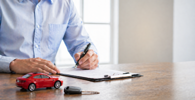 Person signing car insurance paperwork with car keys on a desk