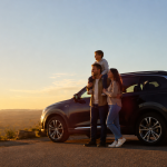 Family standing beside an SUV on a scenic road at sunset