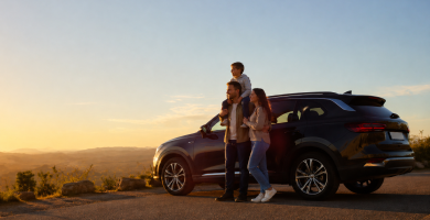 Family standing beside an SUV on a scenic road at sunset