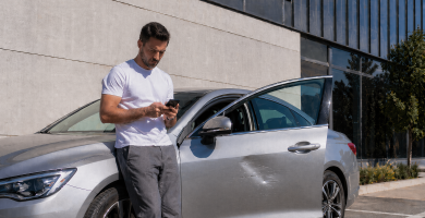 Driver checking a car insurance claim on a phone next to his parked car