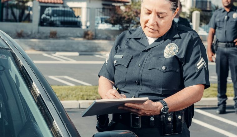 Police officer writing a citation beside a car during a traffic stop
